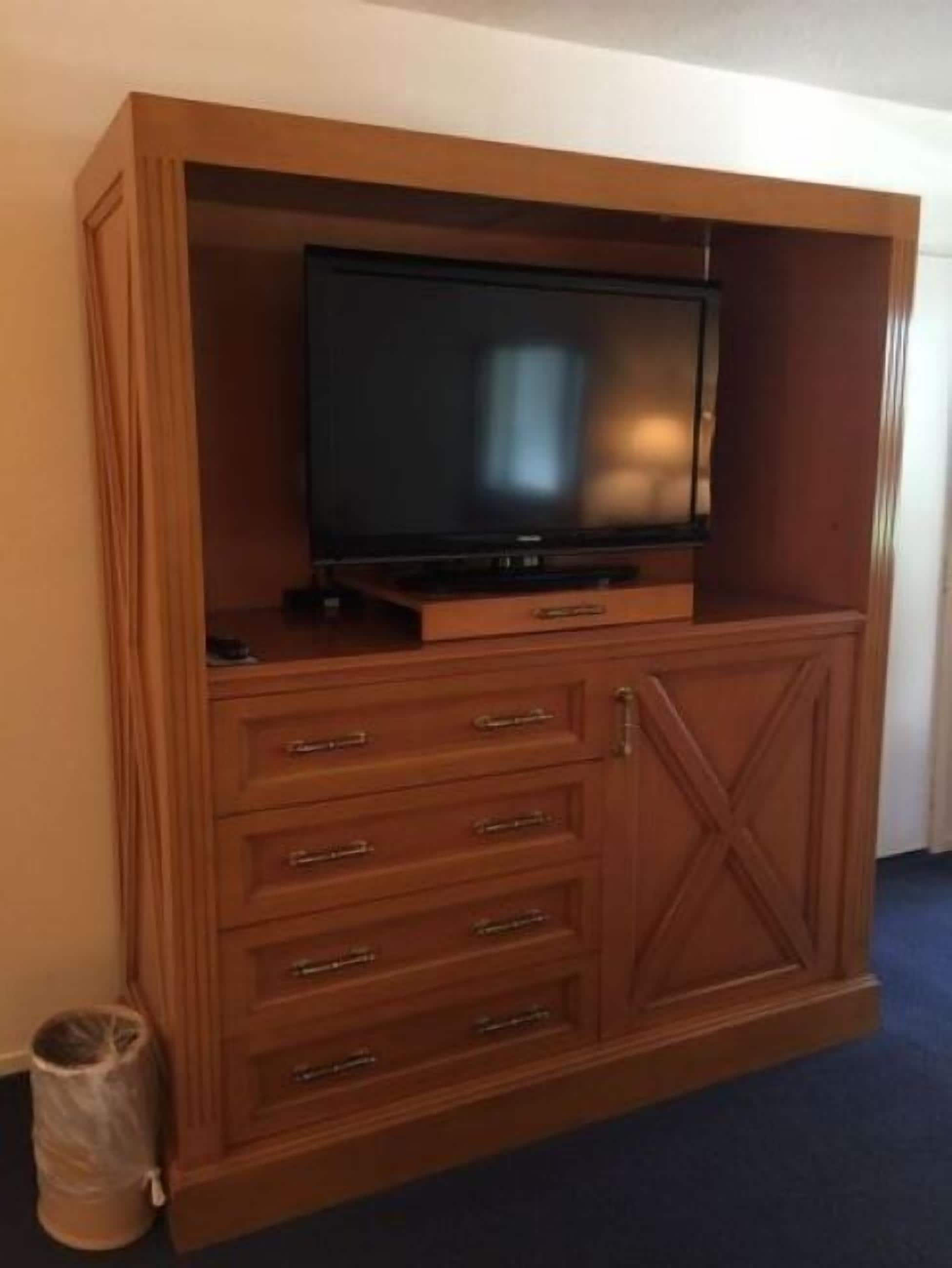 Un mueble de madera con centro de entretenimiento, televisor de pantalla plana, cajones y un cubo de basura.