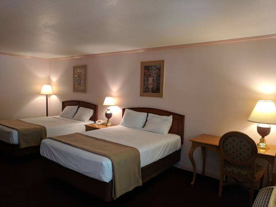 Habitación de hotel con dos camas, un escritorio, una silla y dos lámparas.