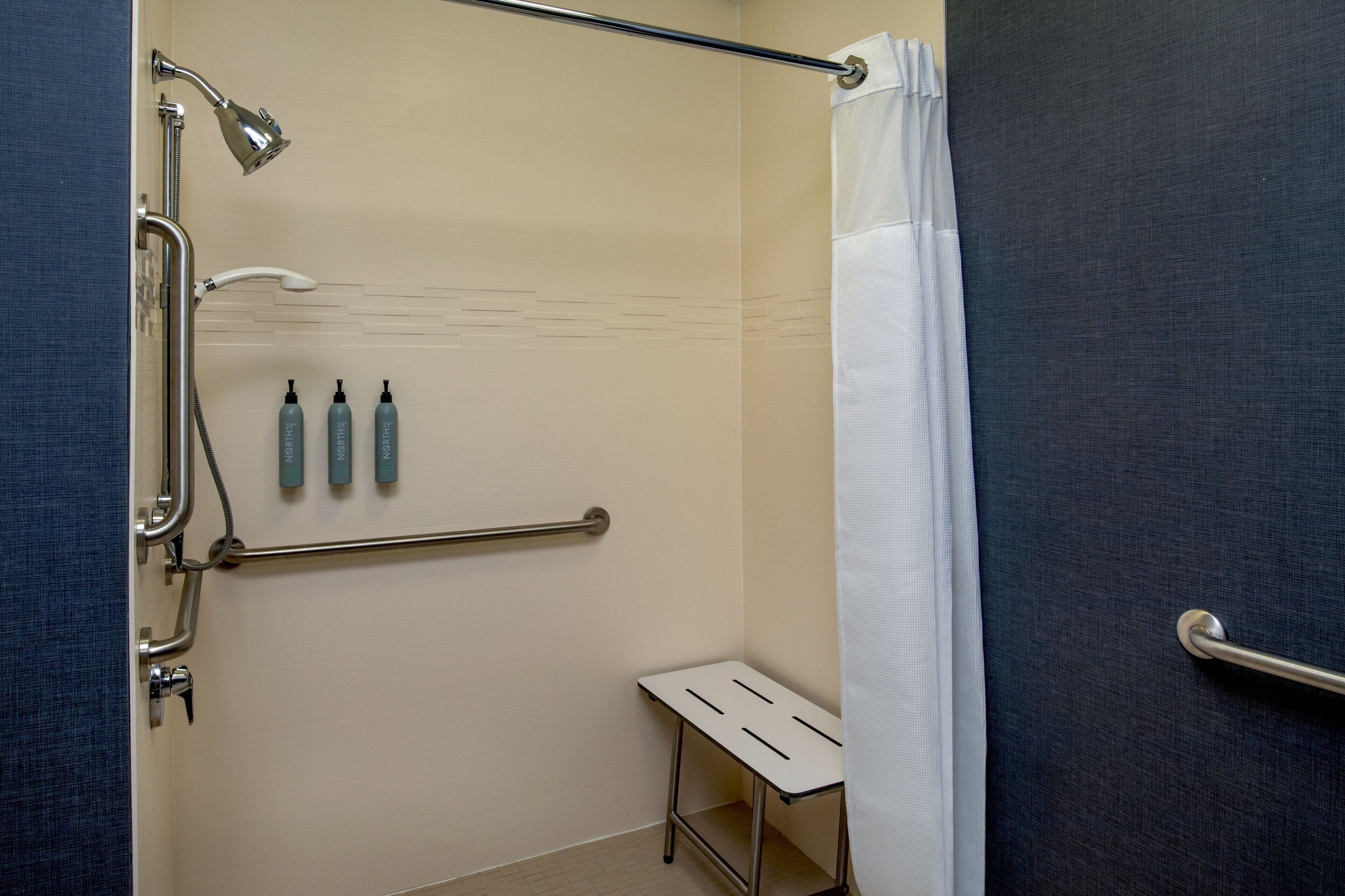 A shower area with a grab bar, a small table, and three bottles of shampoo.