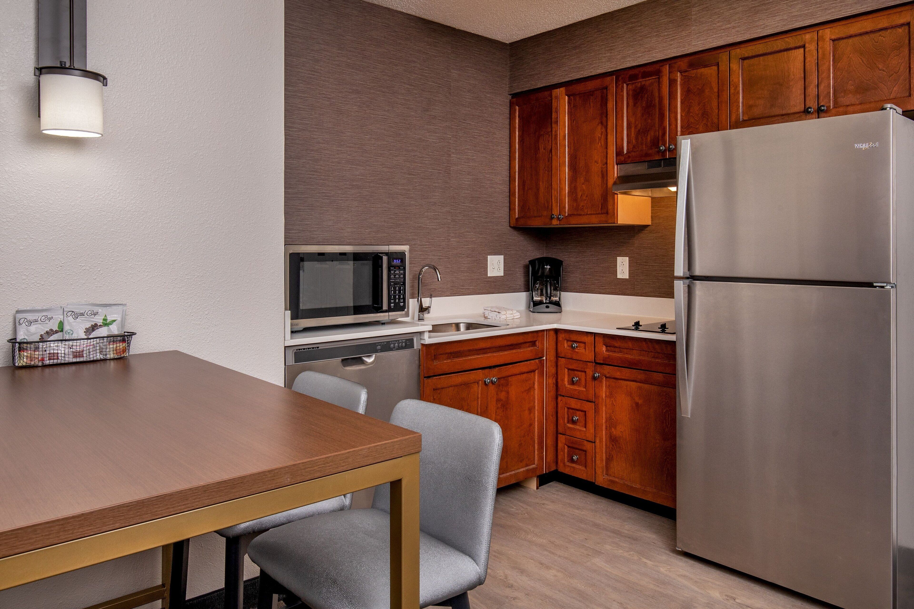 A compact kitchen with wooden cabinets, a stainless steel refrigerator, a microwave, and a coffee maker.