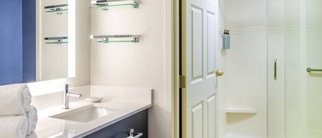 Un baño moderno con lavamanos blanco, espejo y ducha con mampara de vidrio.