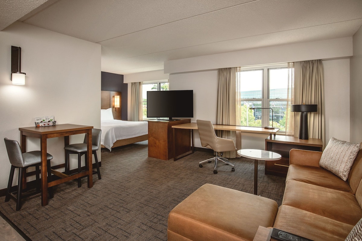 A hotel room with a bed, a desk, a TV, a sofa, and a view of the city.