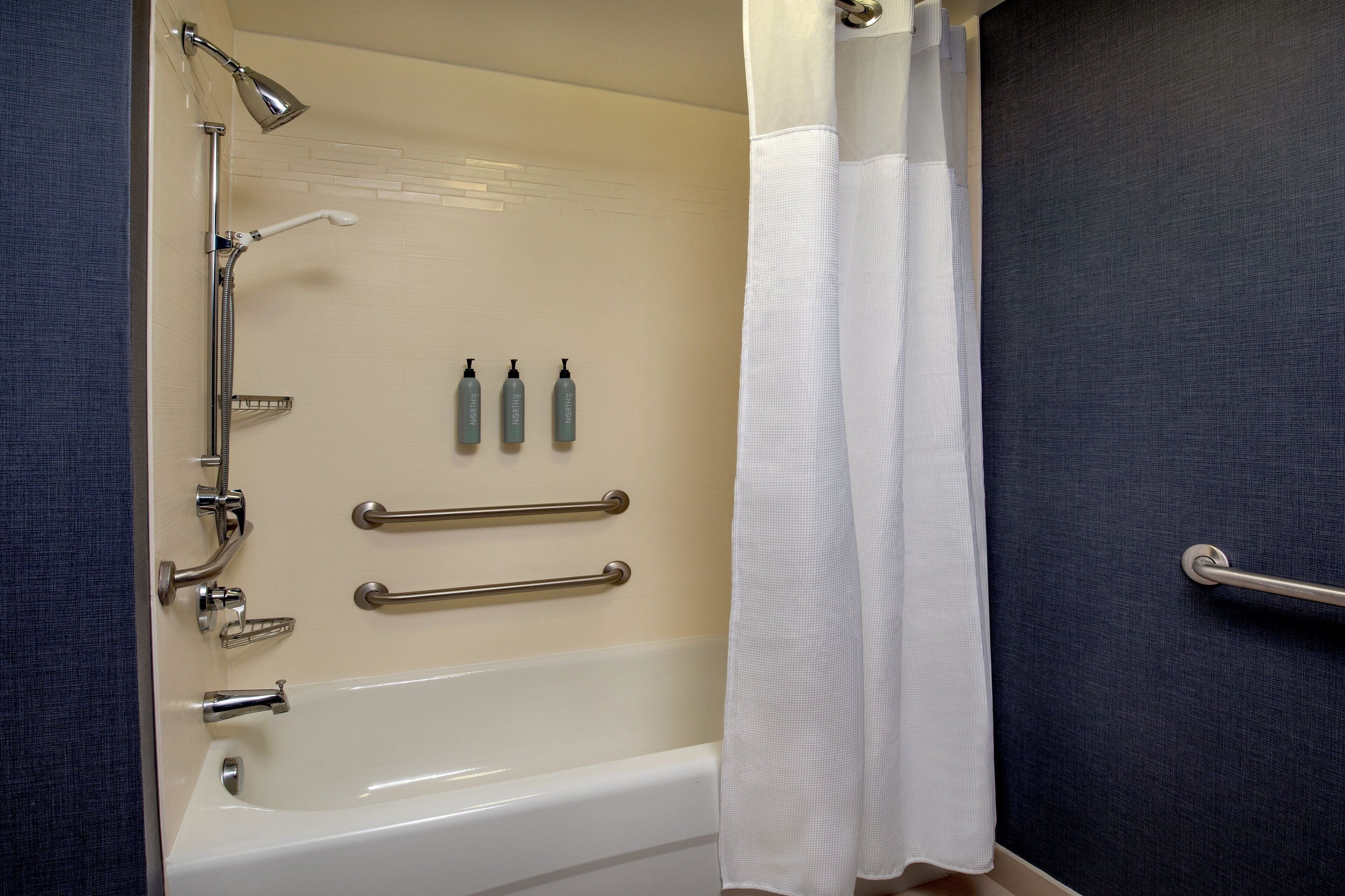 Un bagno con vasca, doccia, maniglioni e articoli da toilette a parete.