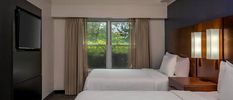 Habitación de hotel con dos camas, televisión, mesita de noche con lámparas y un amplio ventanal con cortinas.