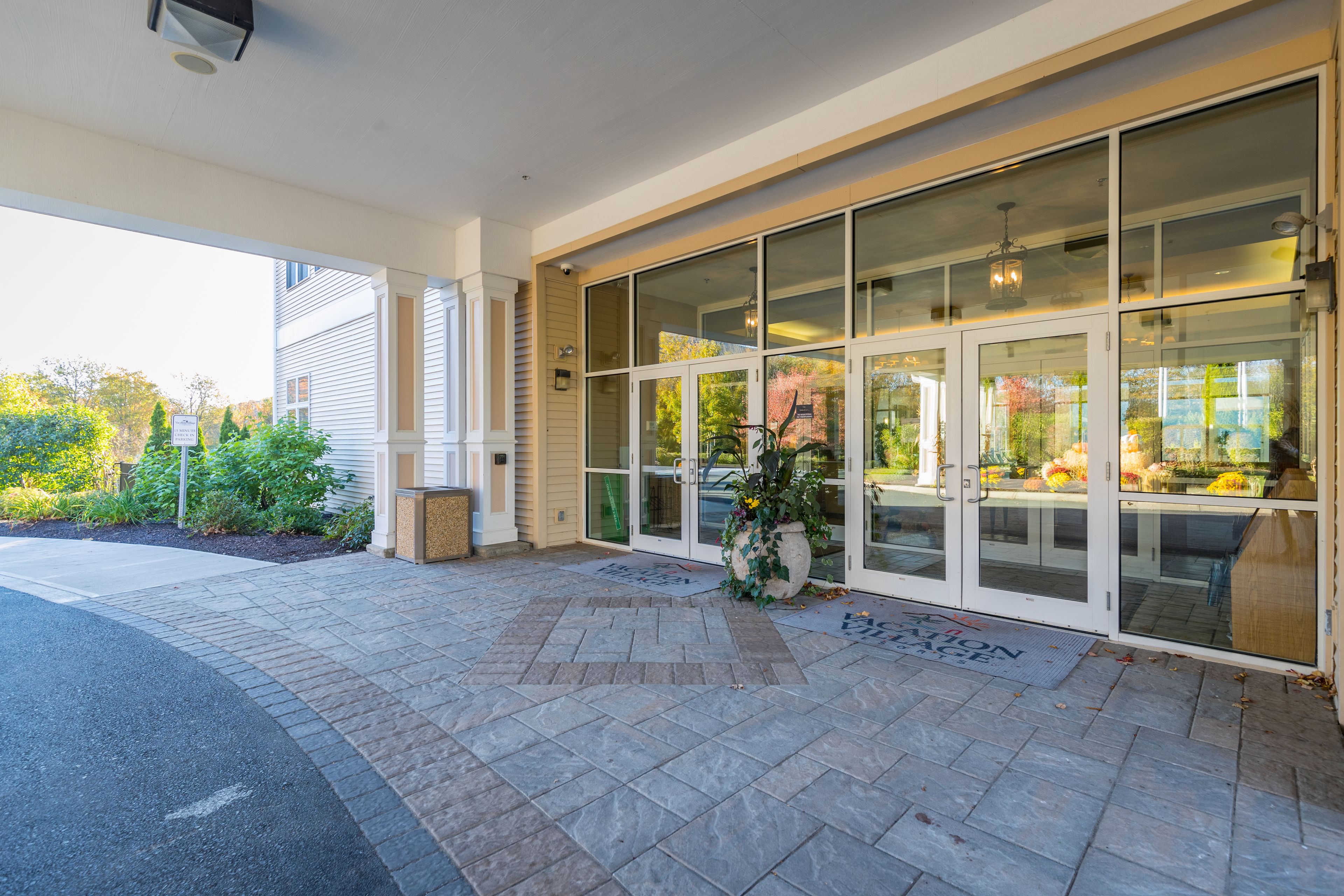 A hotel entrance with a covered patio, large glass doors, and a potted plant.