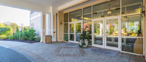 A hotel entrance with a covered patio, large glass doors, and a potted plant.