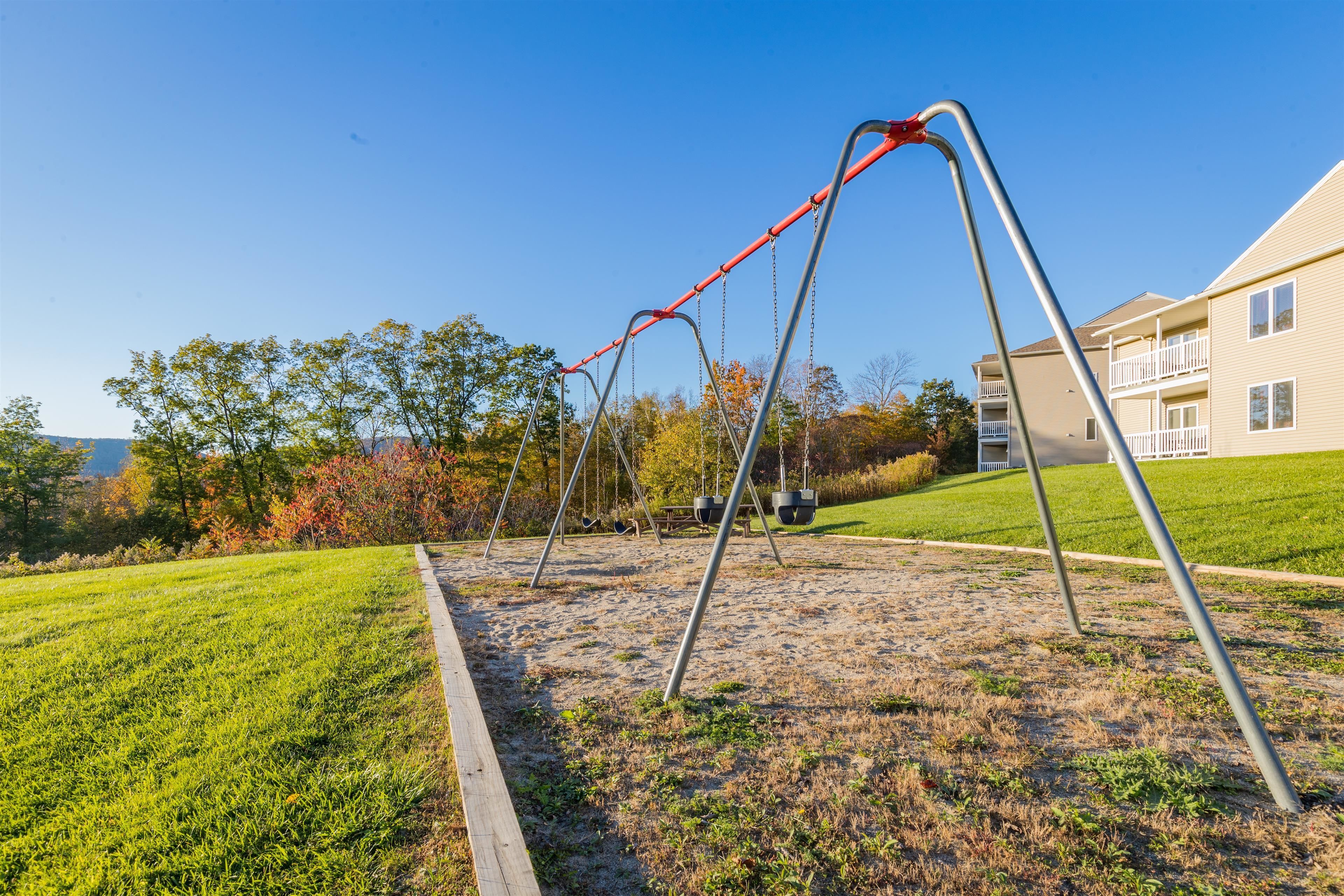 A playground with swings and a sandbox in a grassy area with a building in the background.