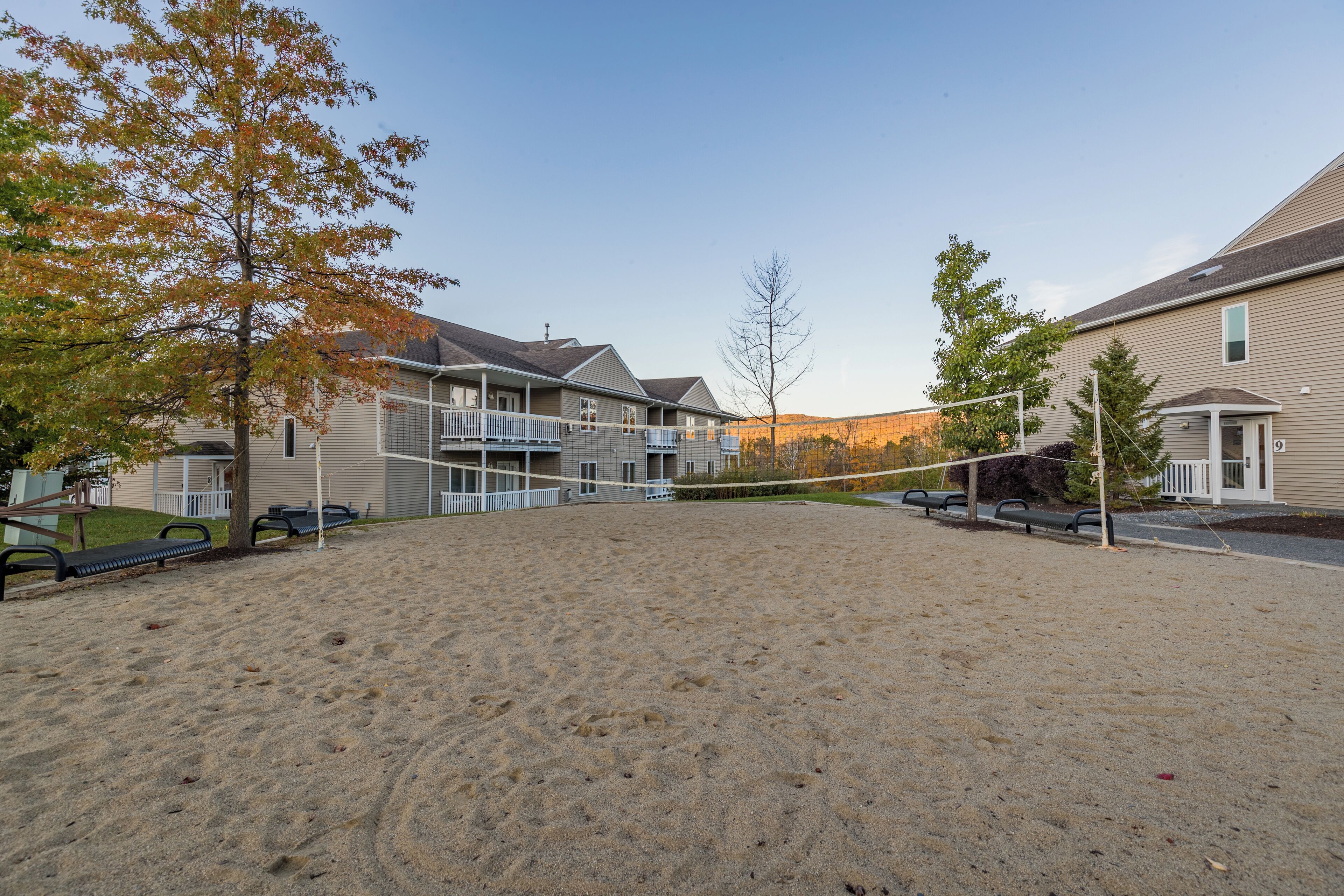 A sandy outdoor area with a volleyball net, surrounded by residential buildings with balconies.