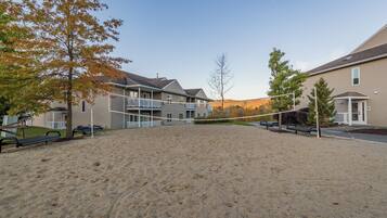 A sandy outdoor area with a volleyball net, surrounded by residential buildings with balconies.