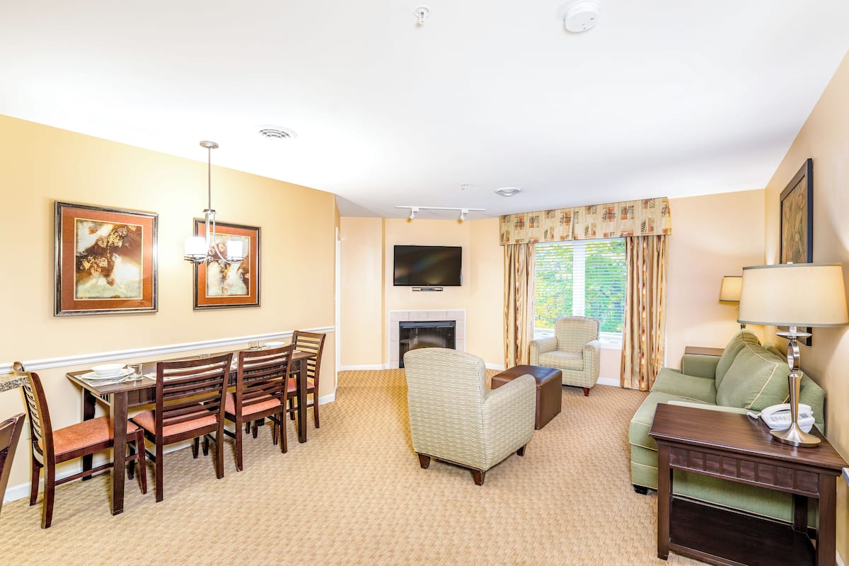 A living room with a fireplace, a dining area with wooden chairs, a sofa, and a television mounted on the wall.