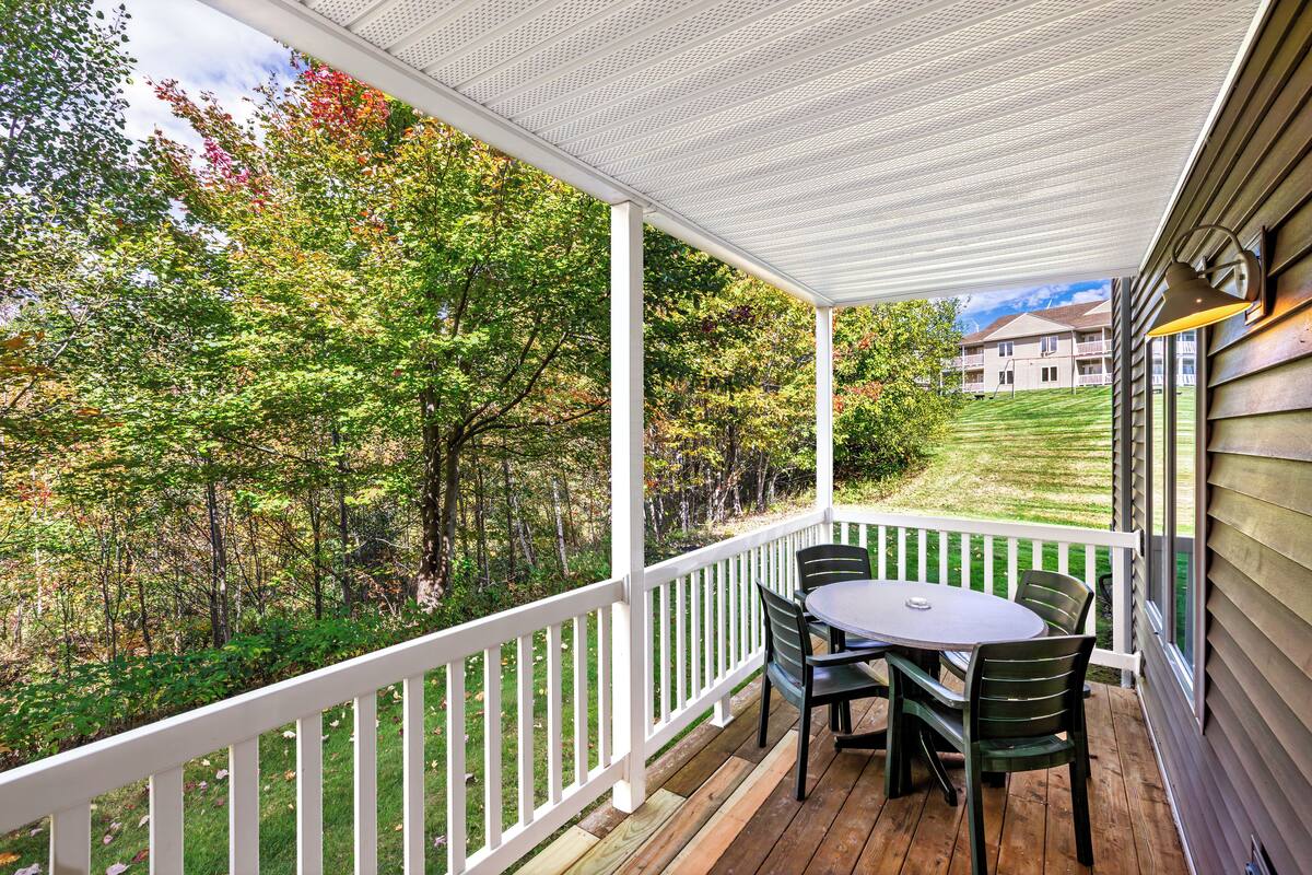 A covered porch with a white railing, a round table, and green chairs.