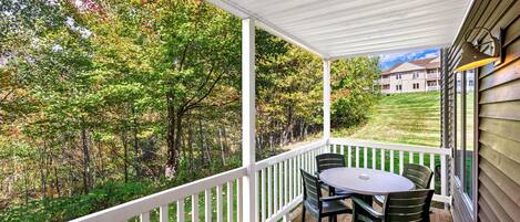 A covered porch with a white railing, a round table, and green chairs.