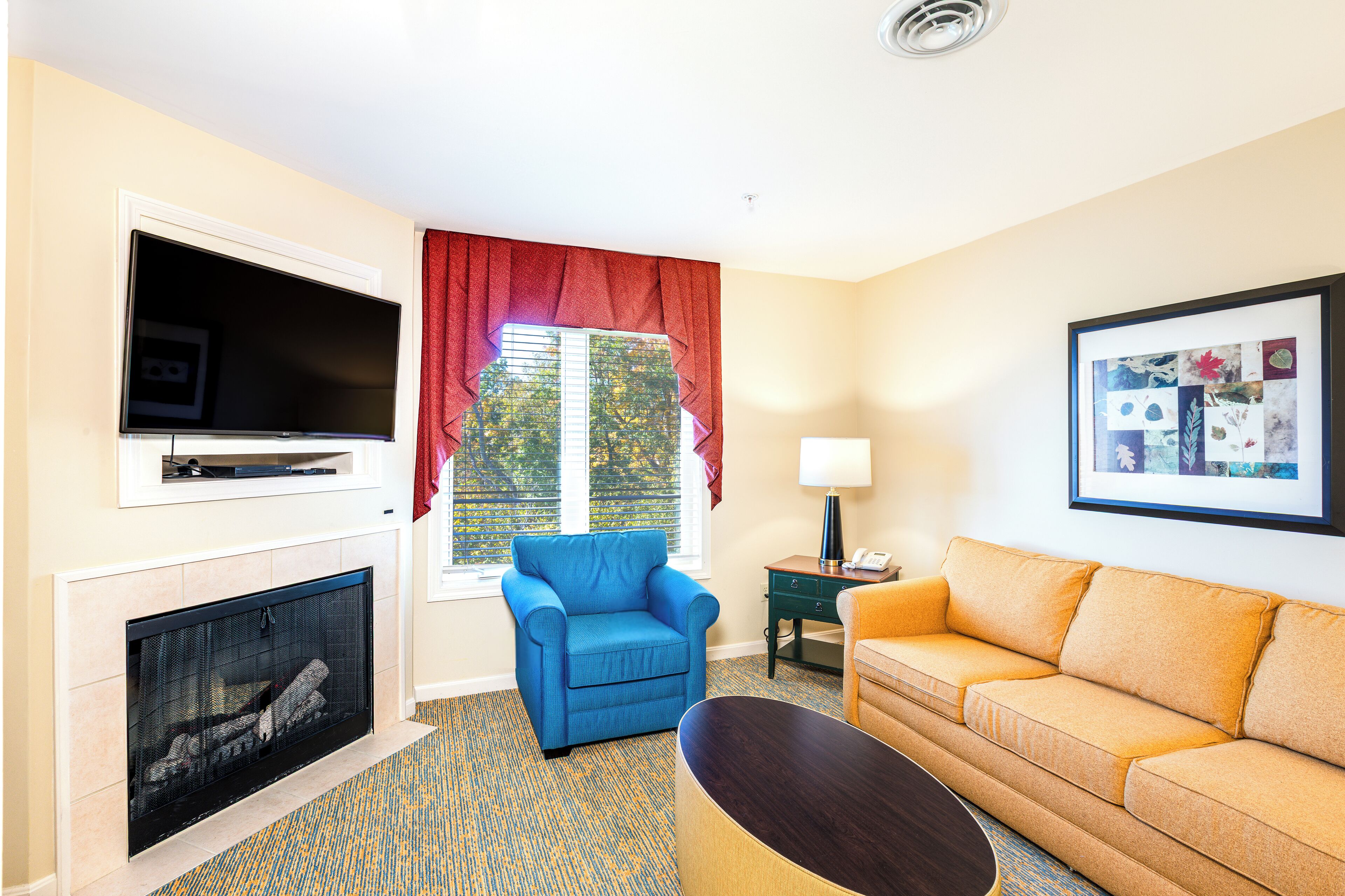 Una sala de estar con chimenea, un sillón azul, un sofá naranja, un televisor y un cuadro en la pared.