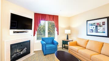 Una sala de estar con chimenea, un sillón azul, un sofá naranja, un televisor y un cuadro en la pared.