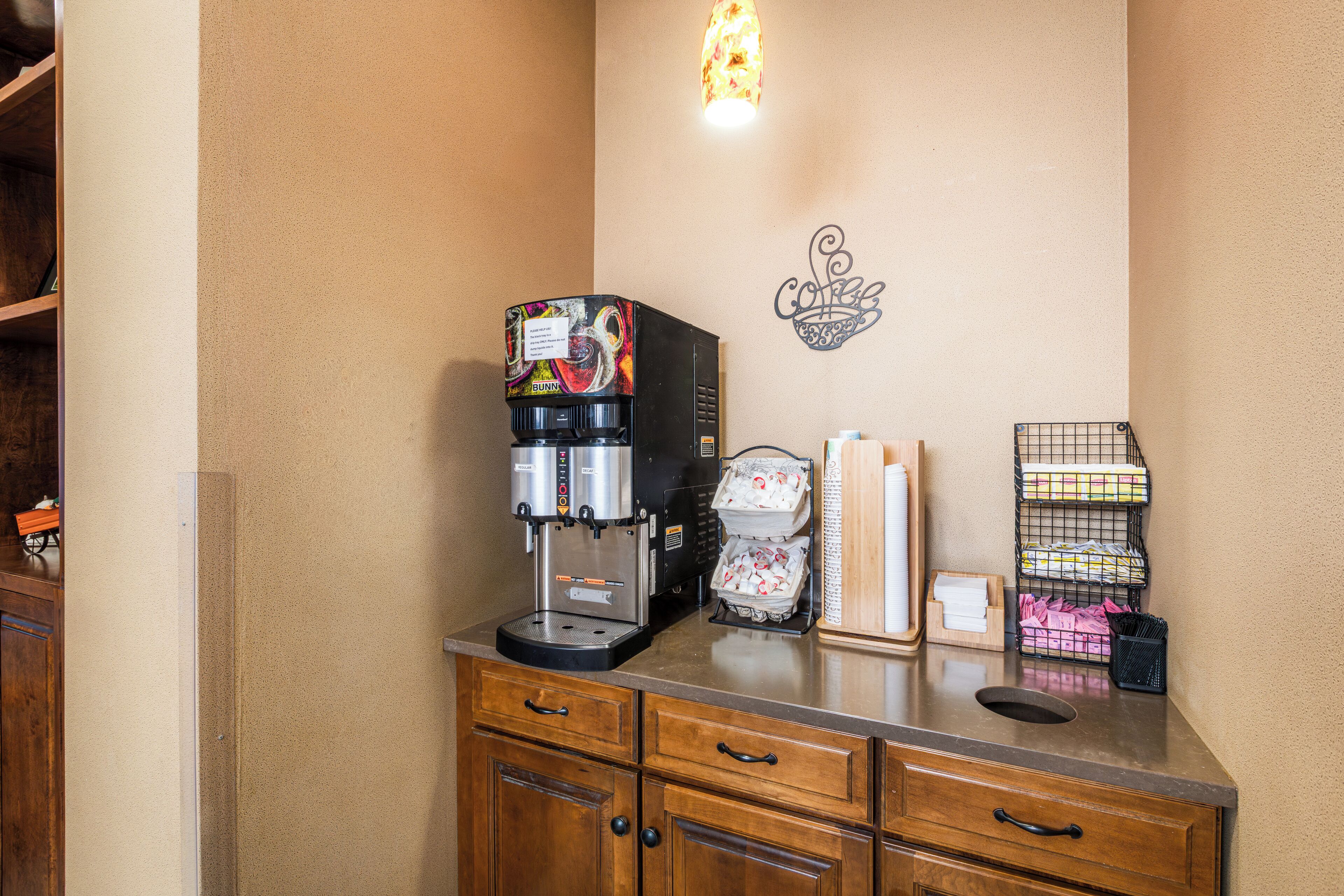 A kitchenette with a coffee machine, a wall-mounted light, and storage shelves.