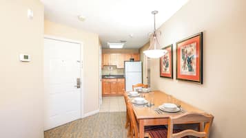 Un comedor con una mesa de madera dispuesta para cuatro, una cocina al fondo y una puerta que da a otra habitación.