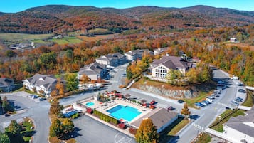 An aerial view of a residential area with a swimming pool, parking, and houses surrounded by autumn foliage.