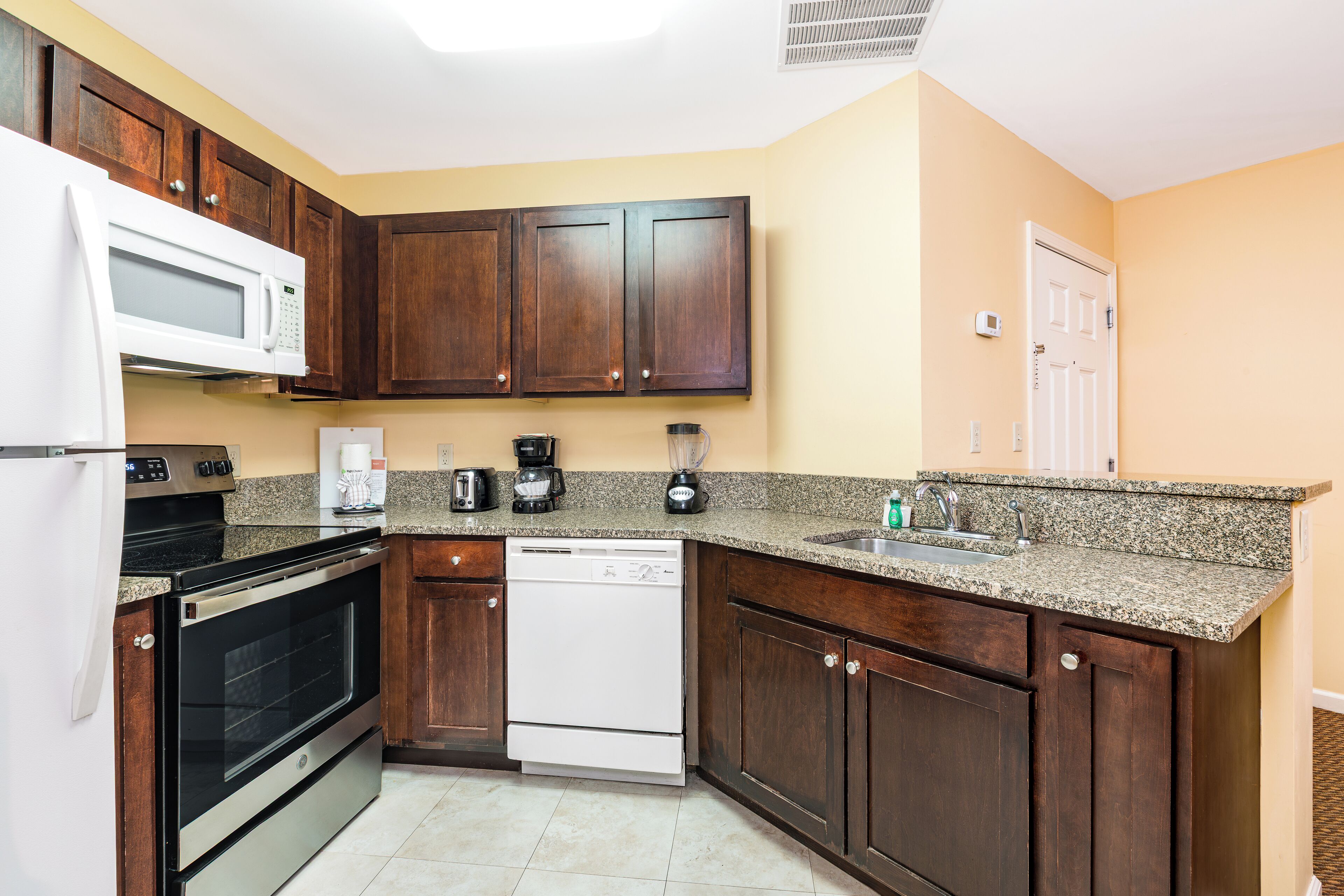 A kitchen with dark wooden cabinets, a white microwave, a dishwasher, and granite countertops.