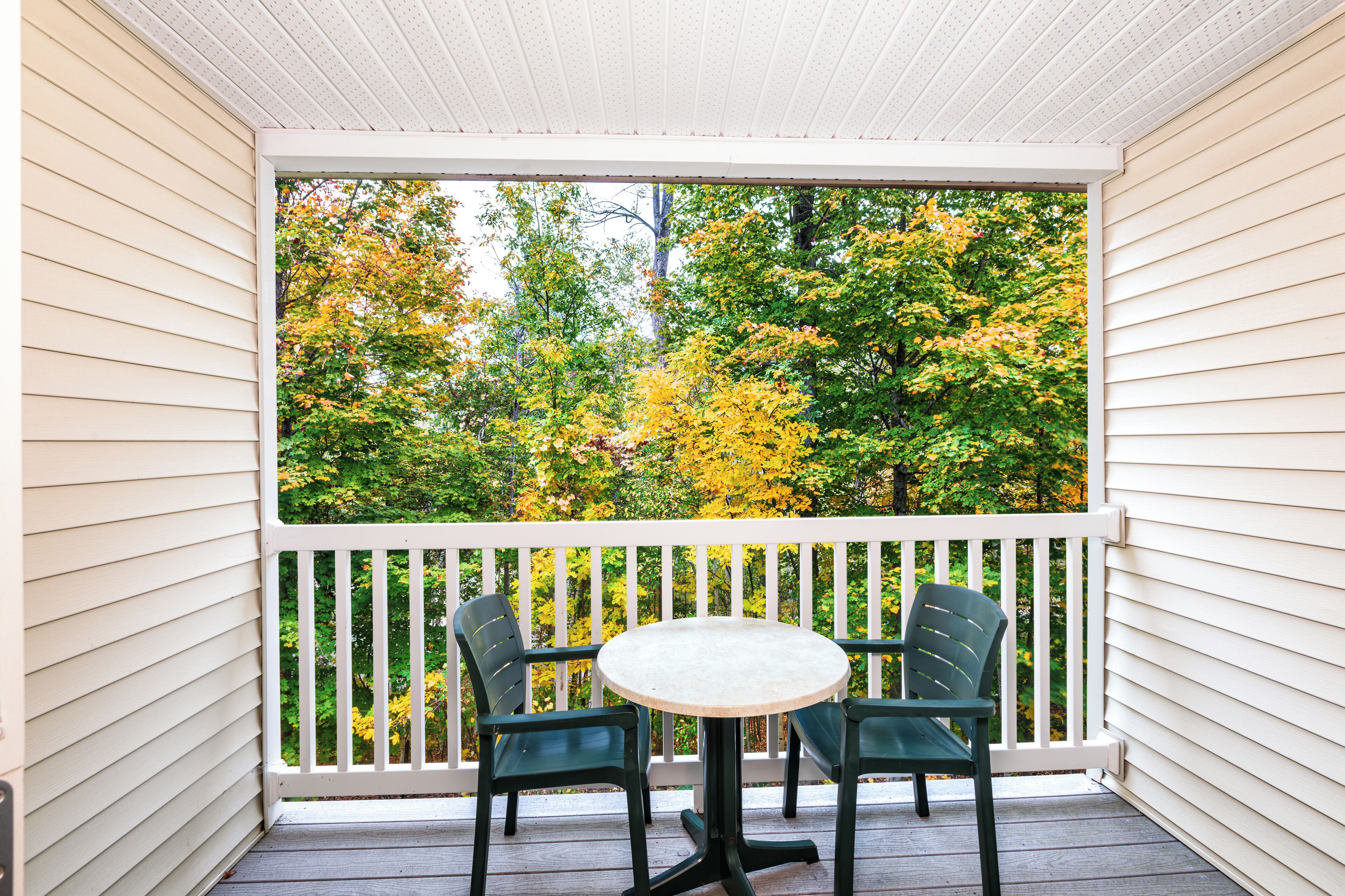 A covered porch with a white railing, two green chairs, and a small round table.