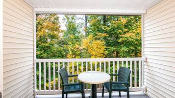 A covered porch with a white railing, two green chairs, and a small round table.