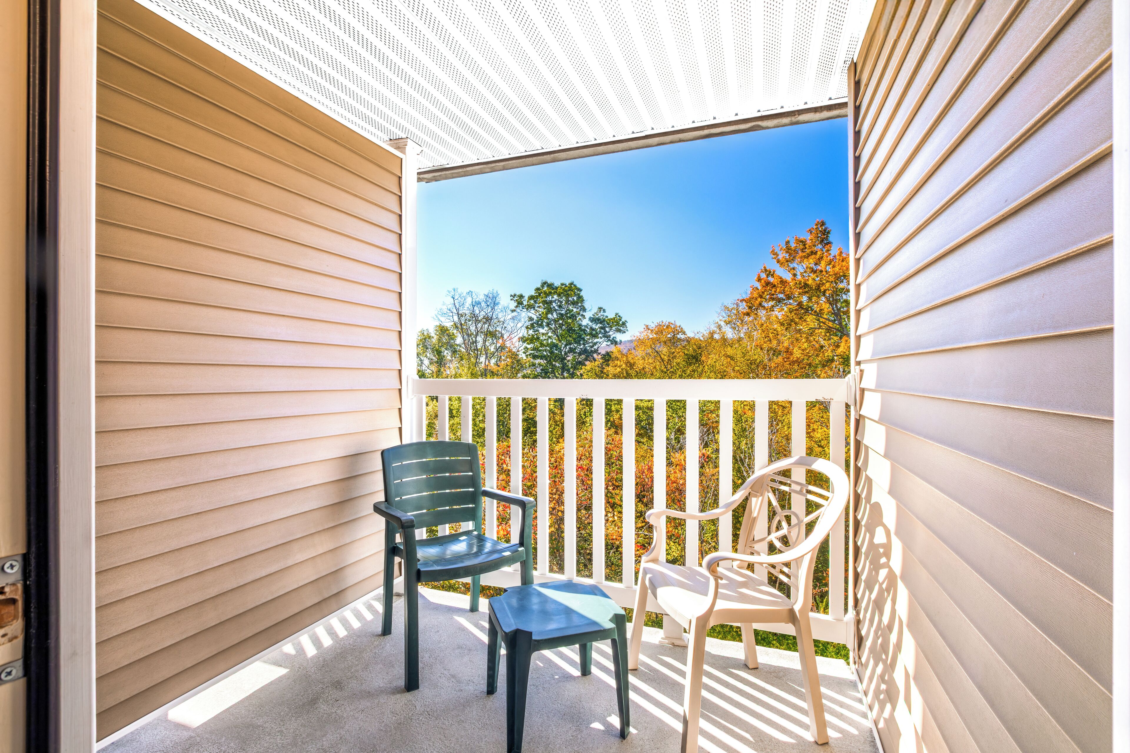 Un balcon avec deux chaises et une petite table, donnant sur une terrasse en bois et des arbres.