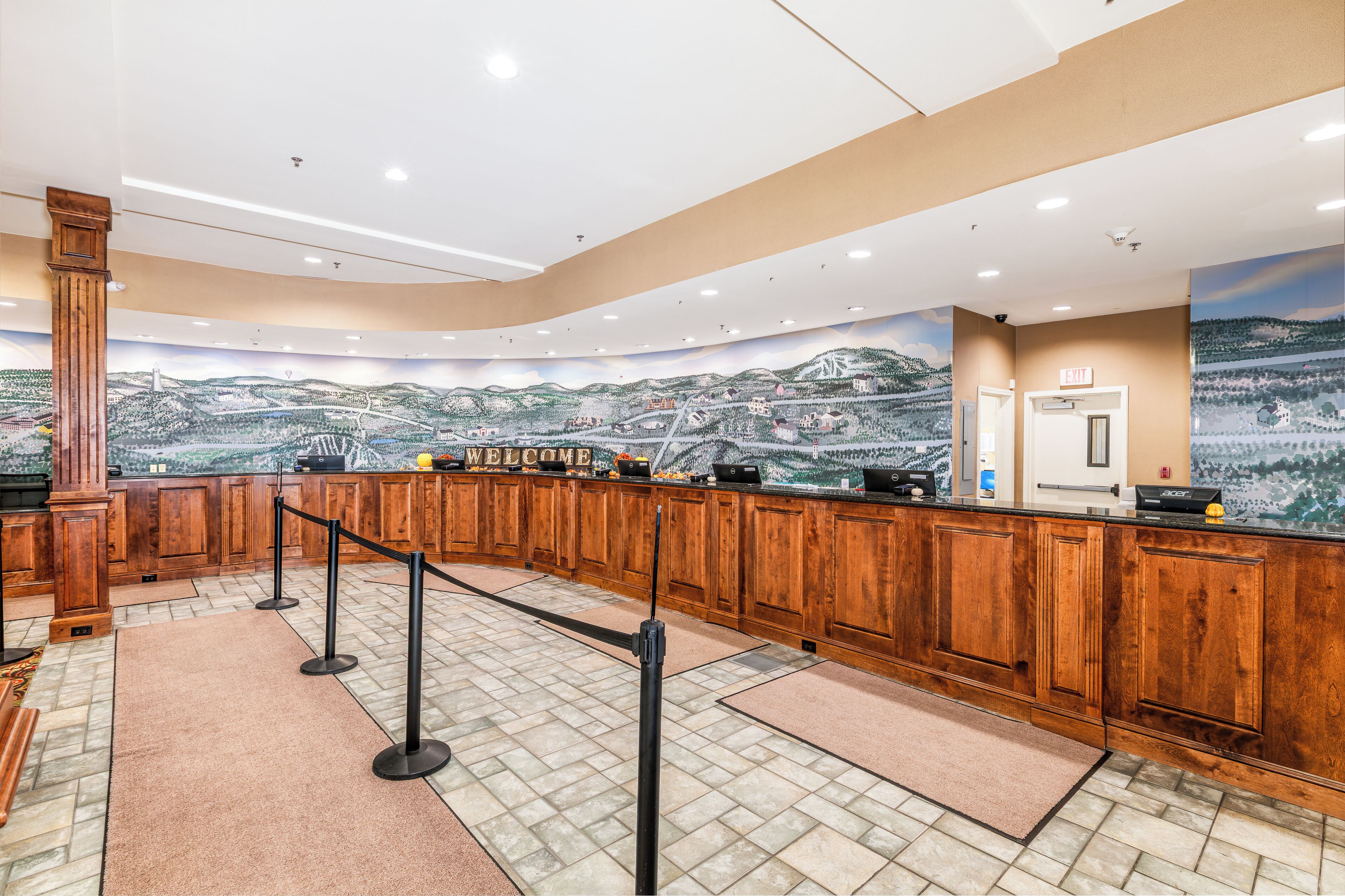 A reception area with a wooden counter, a 'WELCOME' sign, and a mural of a landscape.
