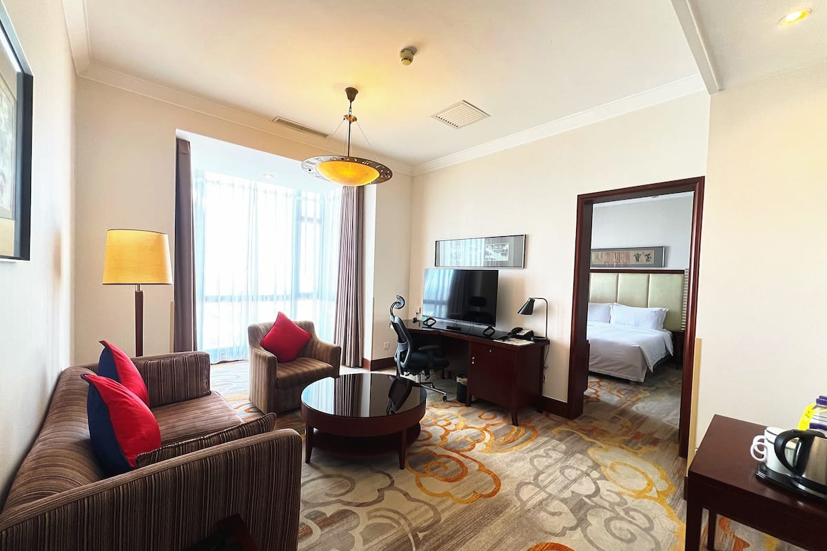 A hotel room with a sofa, armchair, desk, television, and a bed.