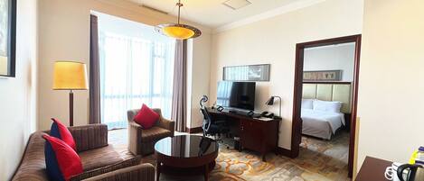 A hotel room with a sofa, armchair, desk, television, and a bed.