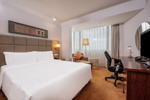 A hotel room with a large bed, a desk, a chair, a lamp, a TV, and a window with curtains.