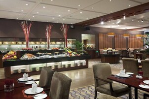 A hotel dining area with a buffet setup, multiple seating arrangements, and a modern interior design.