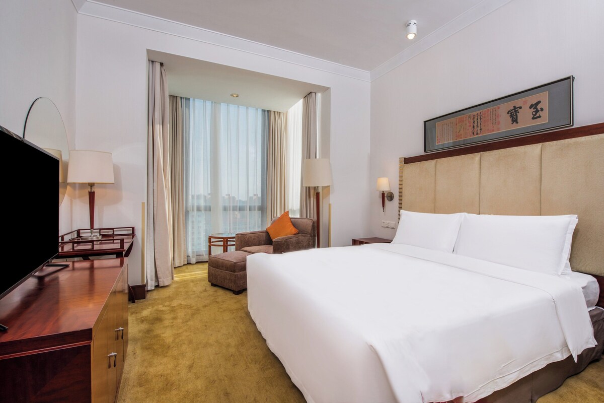 A hotel room with a large bed, a television, a desk, and a chair.