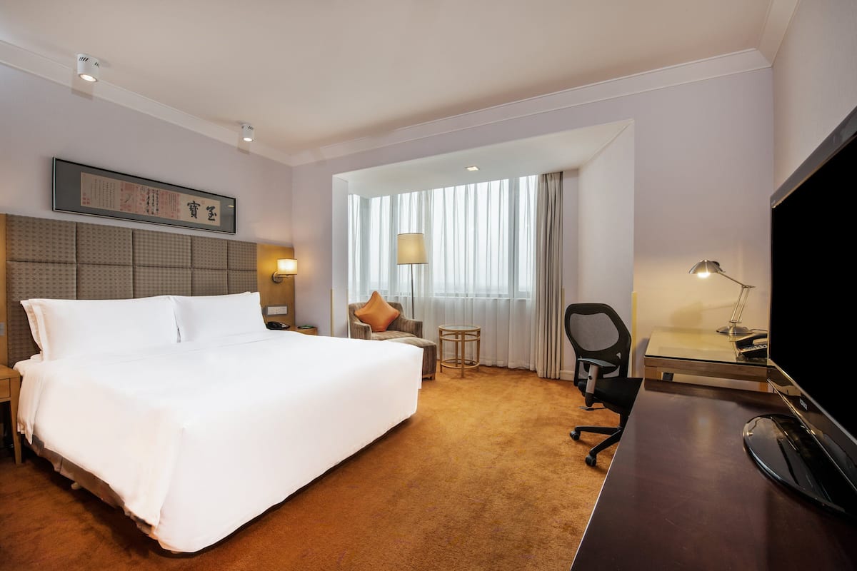 A hotel room with a large bed, a desk, a chair, a TV, and a window with curtains.