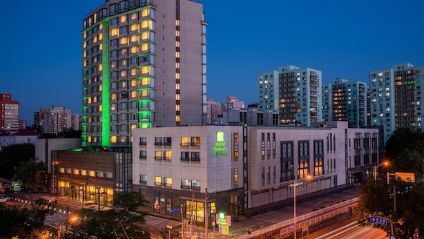 A Holiday Inn hotel with multiple floors, a prominent green sign, and a modern architectural design. - Holiday Inn Beijing Temple Of Heaven by IHG (Beijing)