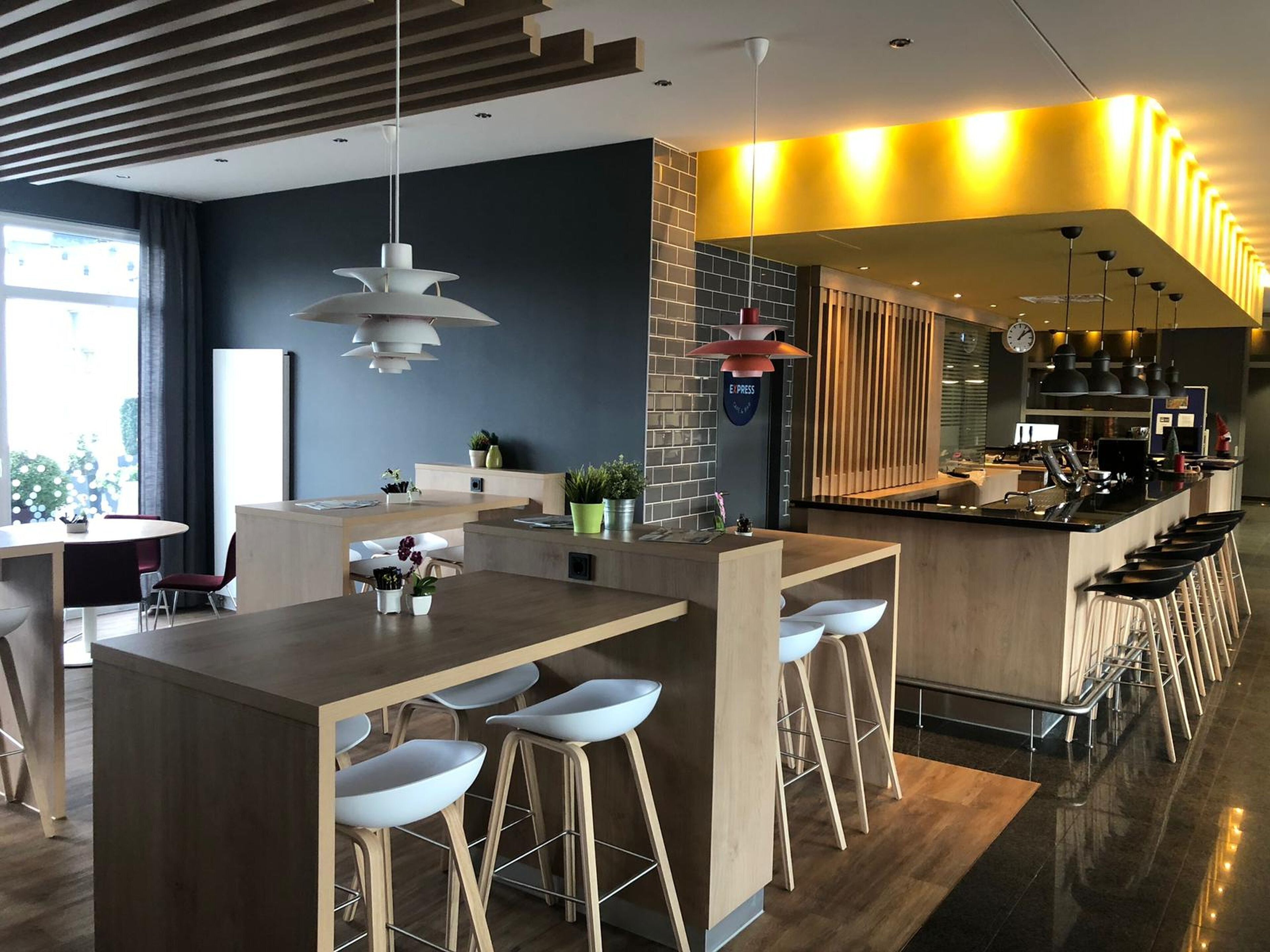 Un área de bar moderna con una barra de madera, taburetes blancos y lámparas colgantes.