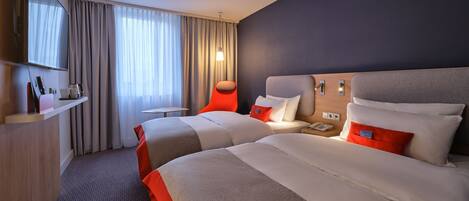 A hotel room with two beds, a TV, a small table, and a chair.