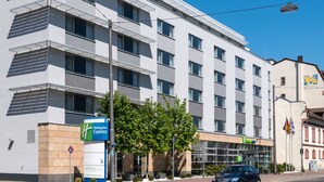 A modern hotel building with a Holiday Inn Express sign, large windows, and a parking sign. - Holiday Inn Express Frankfurt Messe by IHG (Frankfurt)