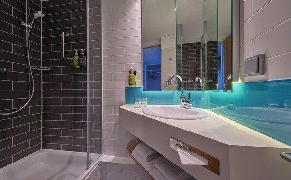 A modern bathroom with a glass shower enclosure, a white sink, and a large mirror. - Holiday Inn Express Frankfurt Messe by IHG (Frankfurt)