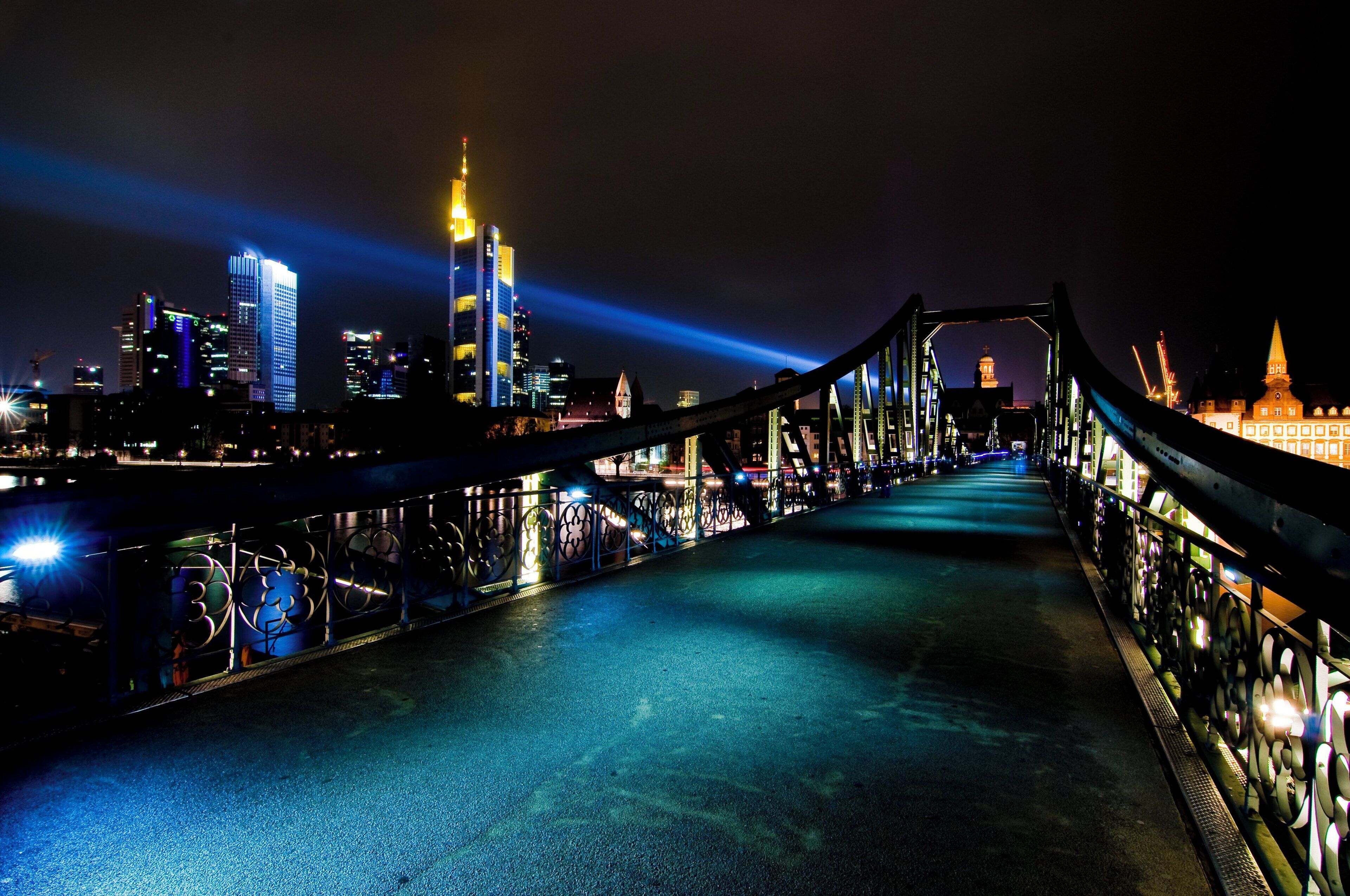 Una vista nocturna de un puente con barandillas iluminadas y un horizonte urbano de fondo.