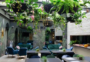 A restaurant with hanging plants, green sofas, and a bar area.