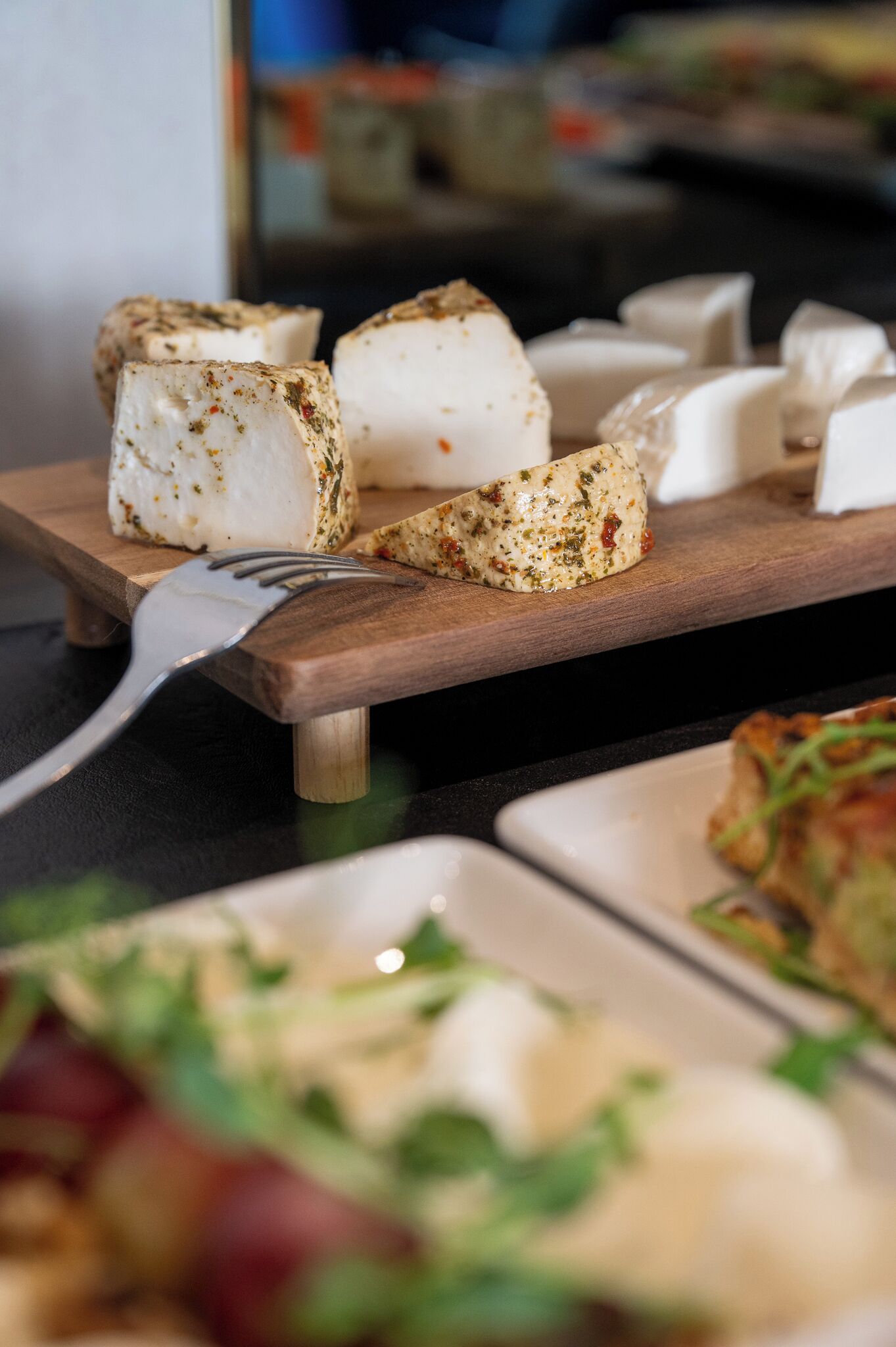 A wooden board with various cheeses and a fork.