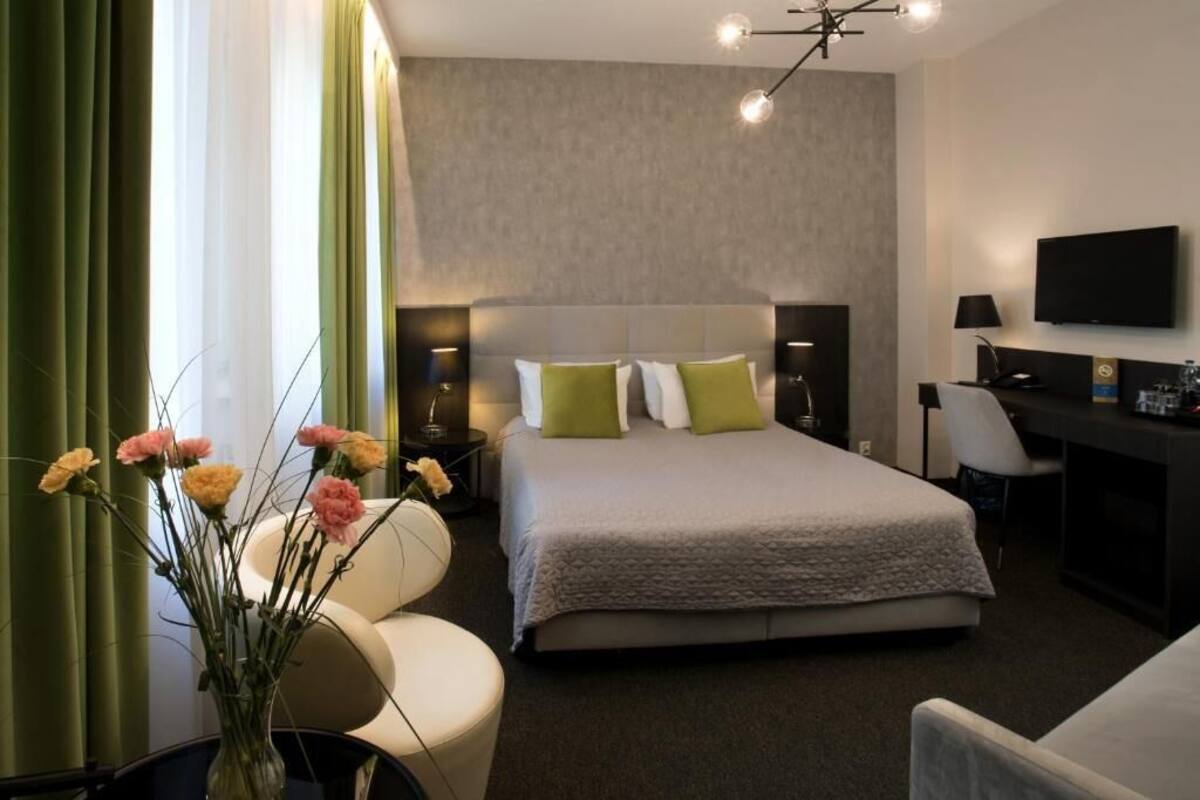 A hotel room with a bed, a desk, a chair, a TV, and a vase of flowers.