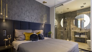 A modern bedroom with a large bed, a bedside table with a lamp, and a glass shower enclosure. - Hotel Atrium (Kraków)