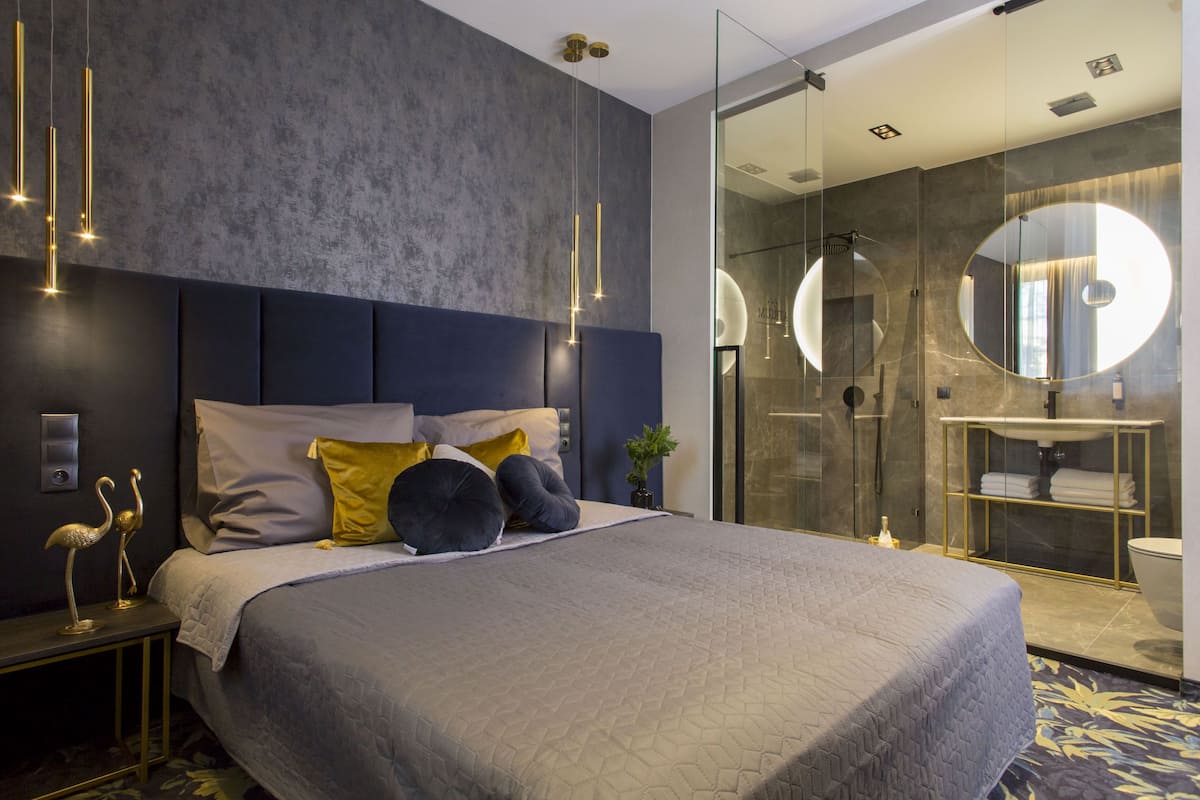 A modern bedroom with a large bed, a bedside table with a lamp, and a glass shower enclosure.