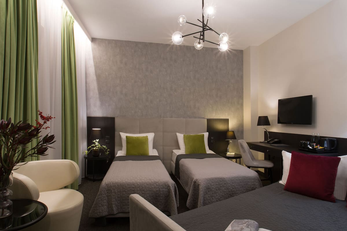 A hotel room with two single beds, a desk with a chair, a television, and a plant.