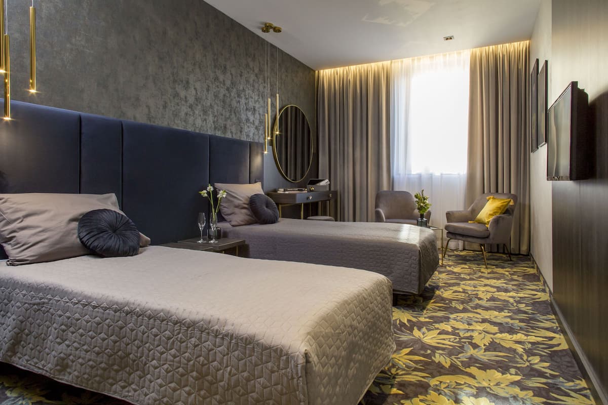 A hotel room with two beds, a desk, a chair, a TV, and a large window with curtains.