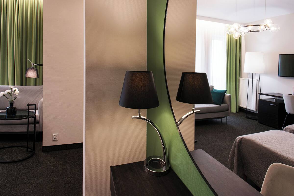 A modern hotel room with a sofa, two lamps, a TV, and a green accent wall.