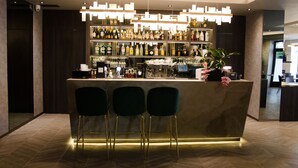 A modern bar area with a marble counter, three black bar stools, and a variety of bottles and glasses on shelves. - Hotel Atrium (Kraków)
