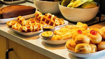A buffet with various dishes including waffles, a loaf of bread, and a bowl of fruit.