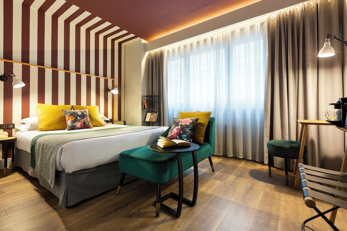 Une chambre d’hôtel moderne, dotée d’un grand lit, d’une petite table, d’un banc et d’un bureau avec une lampe.
