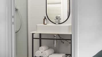 Une salle de bain avec une douche à parois de verre, un lavabo blanc avec un miroir et un porte-serviettes avec des serviettes.